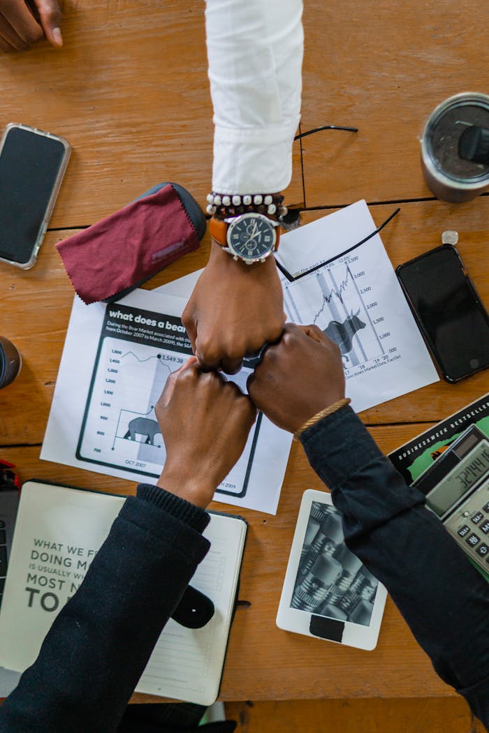 Coworkers joining fists over office desk, symbolizing teamwork and motivation.